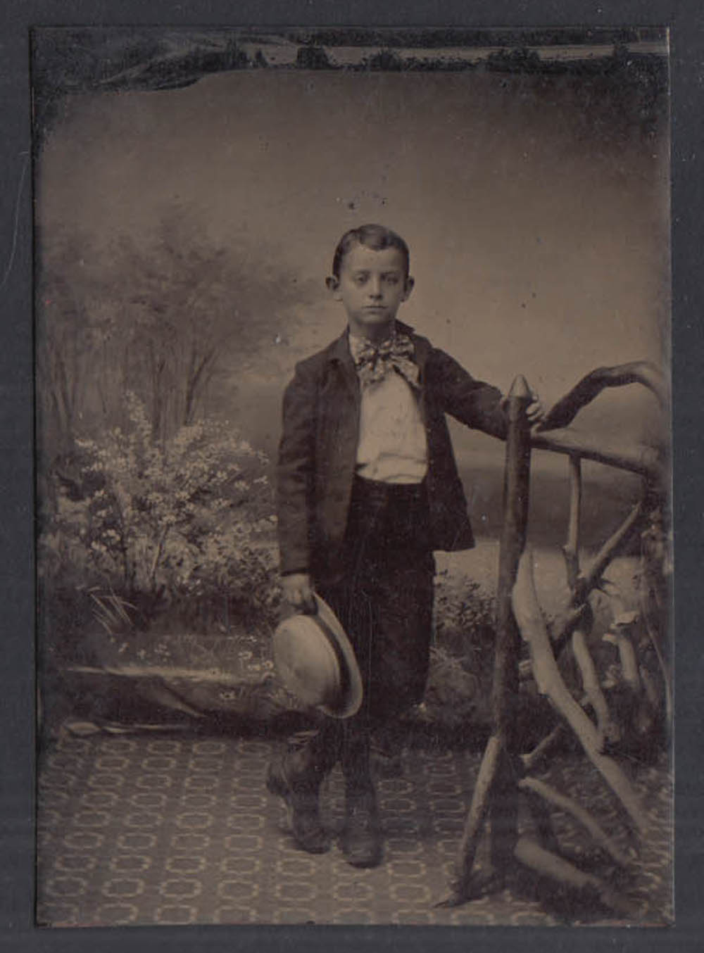 Standing boy holds straw hat big bow tie legs crossed tintype c 1860s